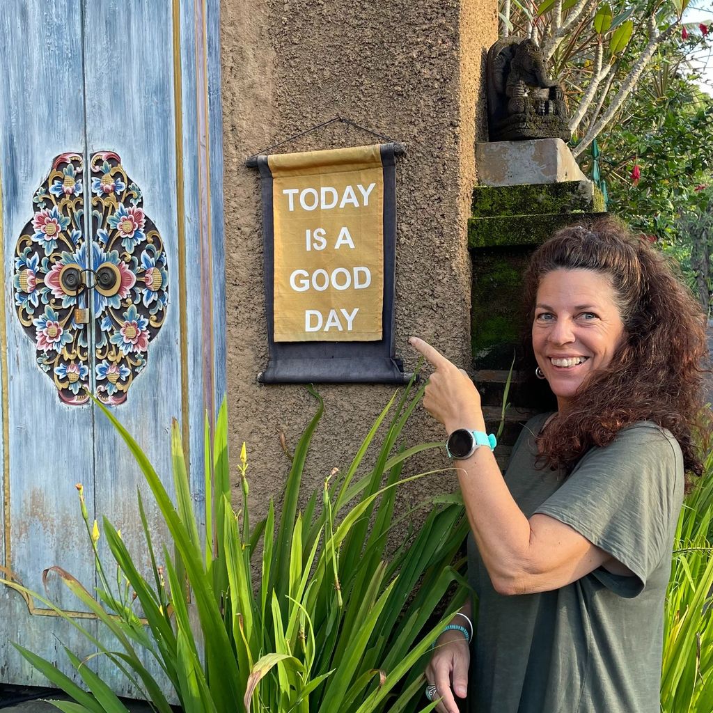 woman in a green top smiling, pointing at a sign that says 'today is a good day'