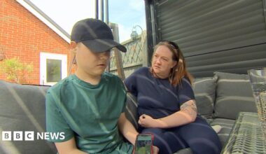Tora sitting on an outdoor sofa in the garden with her son Mason. Mason is wearing a black baseball cap and green t-shirt and is holding a phone. Tora is wearing blue and is looking at Mason.