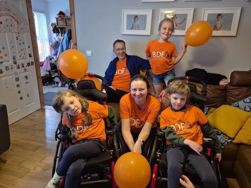 Family with three children, two in wheelchairs, wearing orange t-shirts and holding balloons.