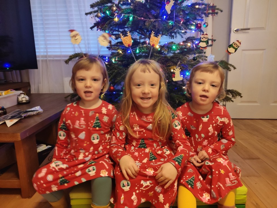 Triplet girls in matching Christmas pajamas in front of a decorated tree.