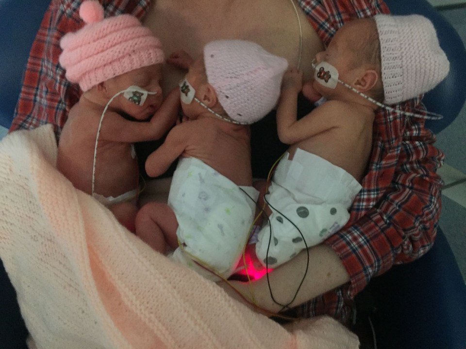 Triplet babies in pink hats held by their mother.