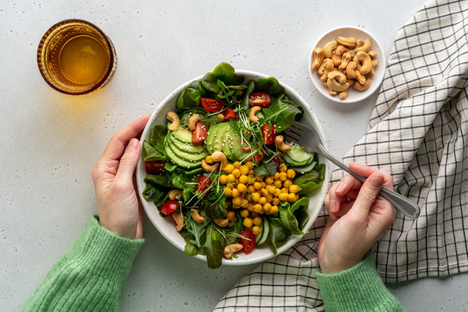 Person eating a vegan salad with avocado, chickpeas, cashews, and other vegetables.