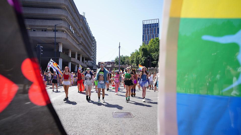 Shot looking between two flags down a city road with people walking in the march - very much dressed for the heat in shorts