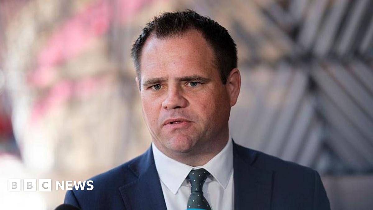 Irish Minister of State Neale Richmond, with short brown hair, wearing a navy suit, white shirt and dark green tie. The background of the image is blurred.