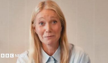 Gwyneth Paltrow appearing in a promotional video for Astronomer. Behind her is a wooden shelf with a plant and a candle on top of it. She is wearing a light blue shirt.