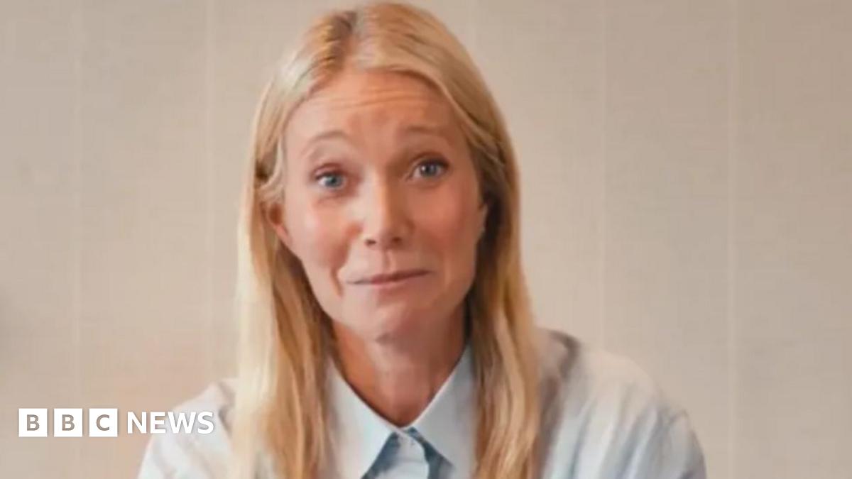 Gwyneth Paltrow appearing in a promotional video for Astronomer. Behind her is a wooden shelf with a plant and a candle on top of it. She is wearing a light blue shirt.
