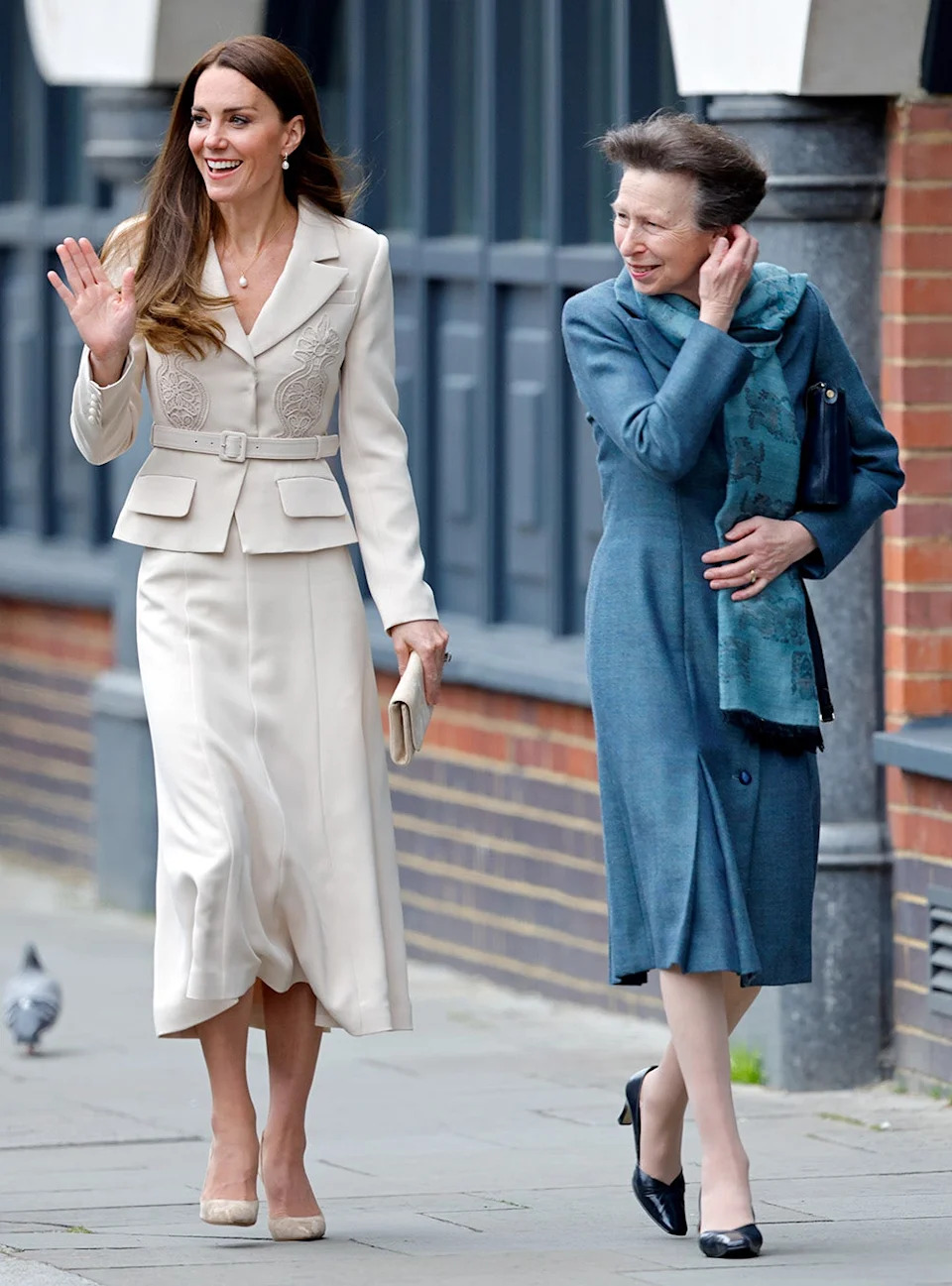 Princess Anne in a blue suit dress walking next to Kate Middleton in a beige suit dress as she waves