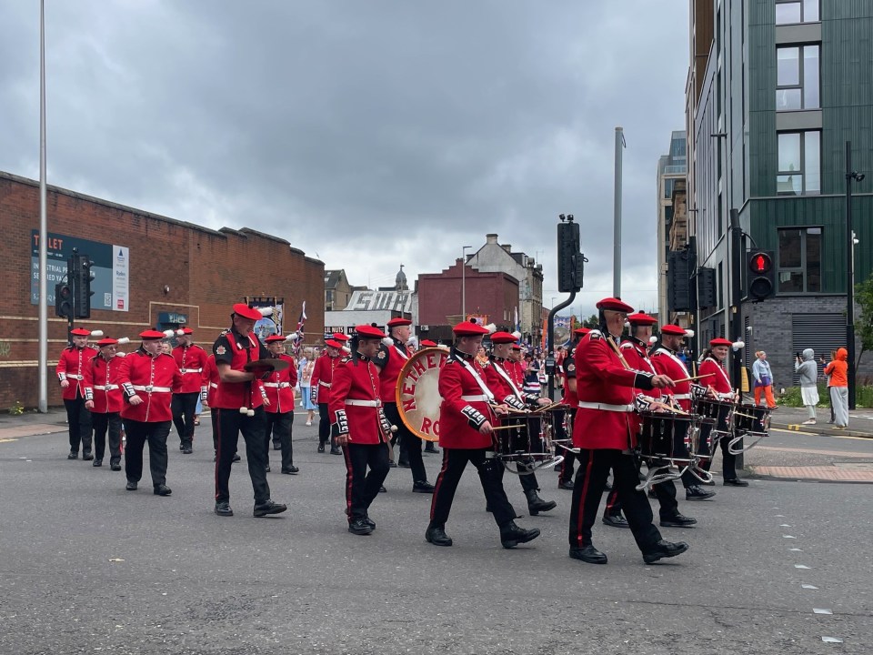 A marching band in red uniforms plays at an Orange Order parade.