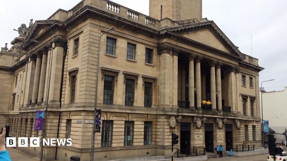 The Guildhall is made of stone and has four large pillars that hold up an apex roof above a balcony on the first floor.  It is a grand building with large black windows.