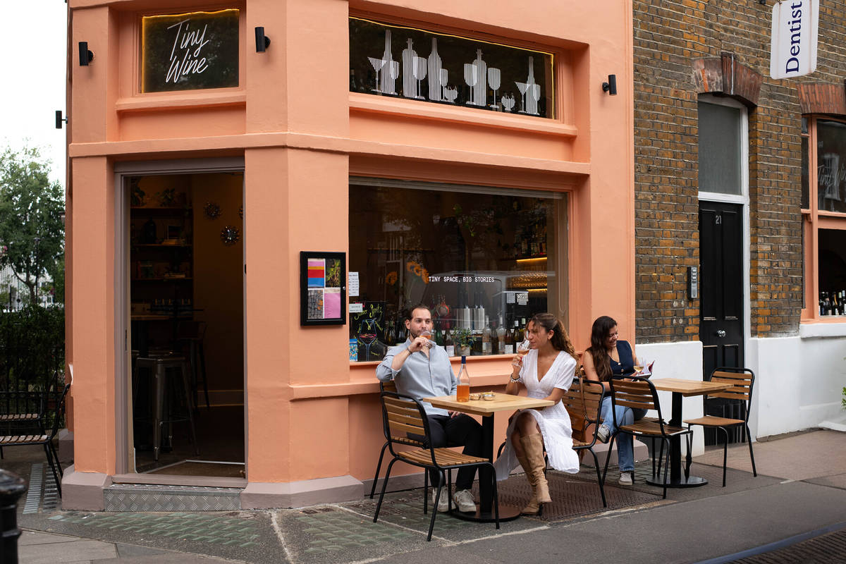 people sat at outside tables outside a peach hued wine bar