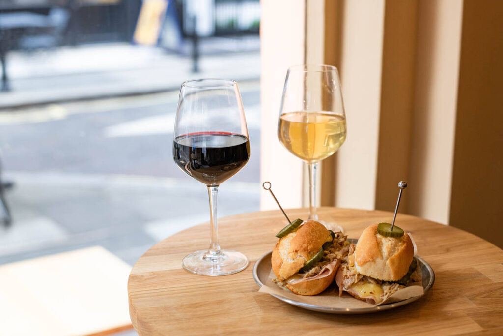 two mini sandwiches on a plate next to two glasses of wine - one red and one white