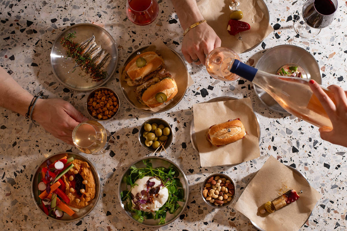 a table covered in tapas dishes and glasses of wine with hands reaching out for food and filling up wine glasses