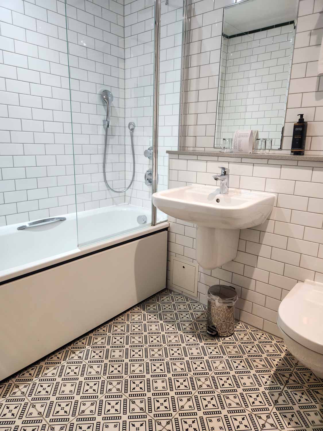 Bathroom with geometric patterened floor tiles, bath and overhead shower - my Mercure Grand Bristol hotel review