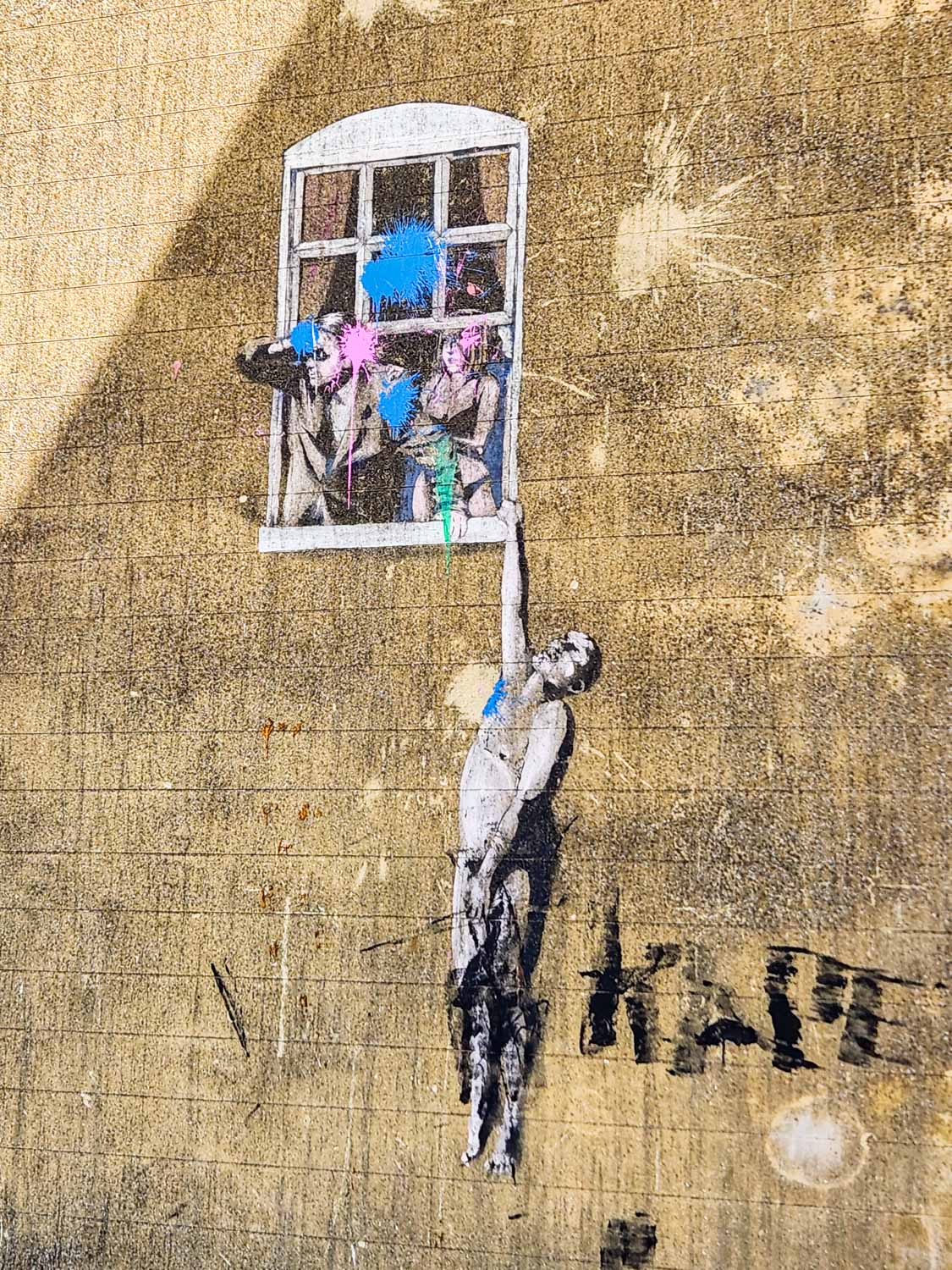 Banksy image of a naked man hanging from a window with a suited man looking out and a woman in underwear behind him, now covered with blobs of paint - one of the sights from a walking tour of Bristol with kids