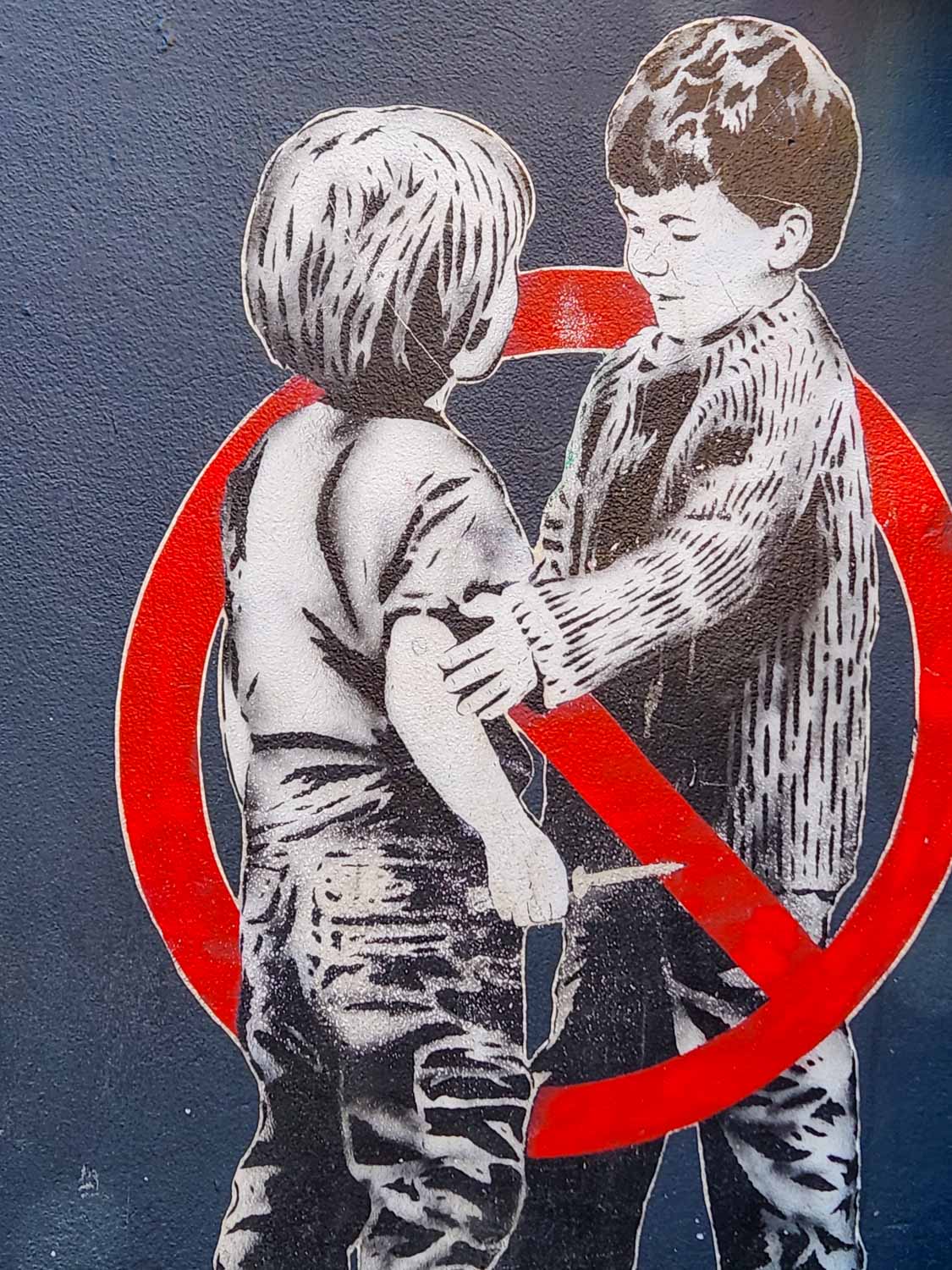 Two young boys, one holding a knife, in a piece of street art from JPS - one of the sights from a walking tour of Bristol with kids