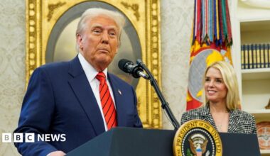 Donald Trump wears a blue suit, red tie with Pam Bondi standing next to him