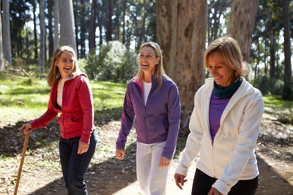 Three women, aged 40-50, walking along and laughing together on a forest walk