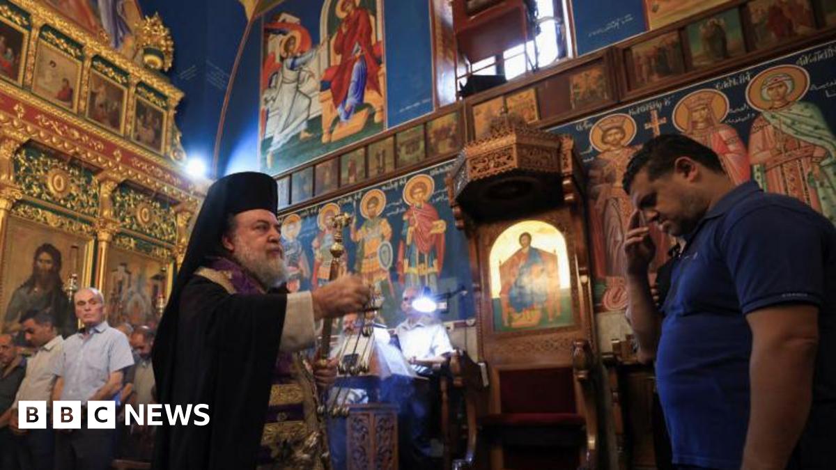 A priest stands in the Holy Family Church in Gaza as a mourner receives blessings during a funeral for those killed in the strike - 17 July 2025