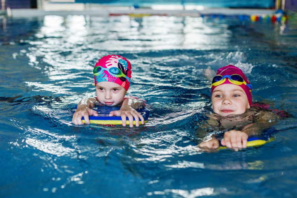 Two girls learning to swim in a pool using swim boards.