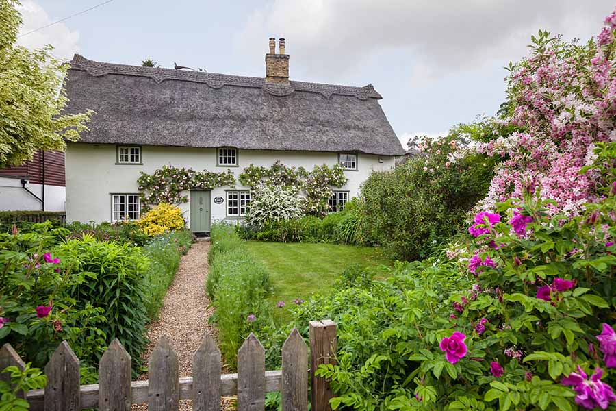 A traditional English country cottage with thatched roof, green lawns and colourful flowers