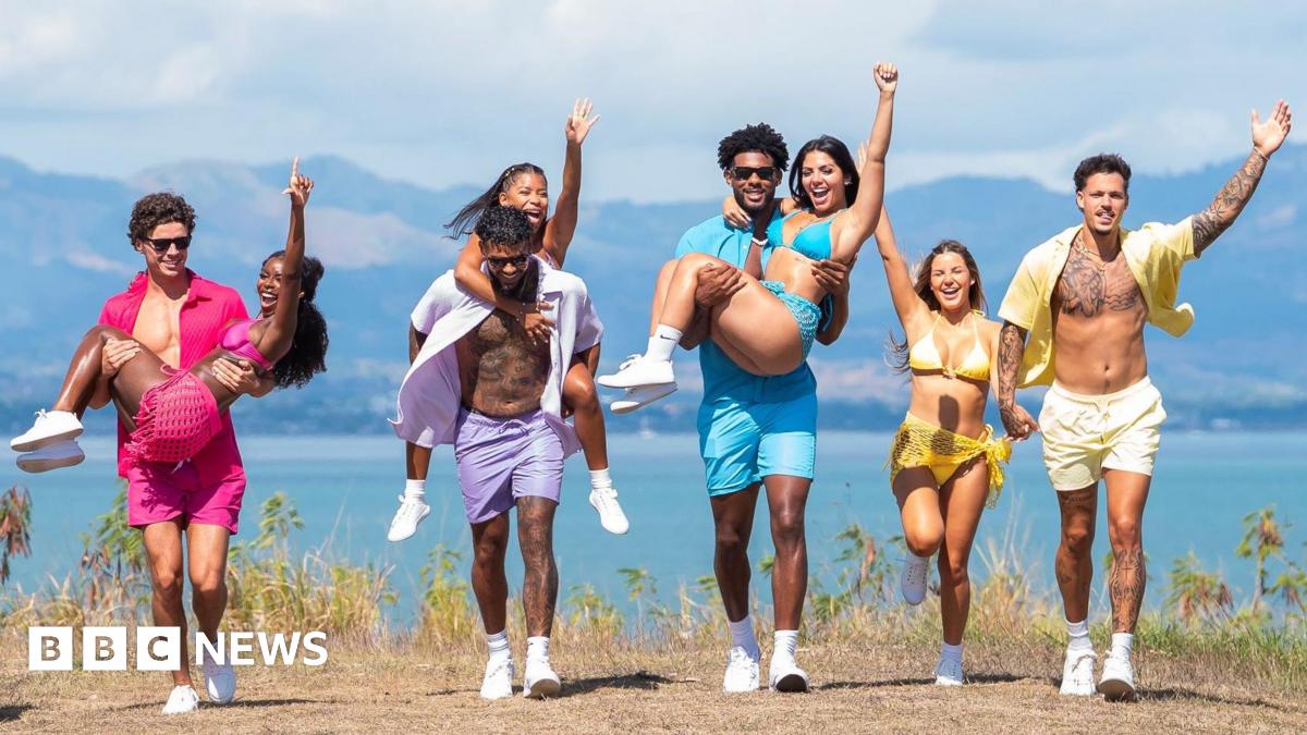 L-R Love Island finalists Nicolas "Nic" Vansteenberghe, Olandria Carthen, Bryan Arenales, Amaya Espinal, Chris Seeley, Huda Mustafa, Iris Kendall, Jose "Pepe" Garcia-Gonzalez. The couples are pictured wearing matching coloured outfits while walking along the coast on a sunny day, the sea and mountains behind them. Nic, Bryan and Chris all carry their partners while Iris and Jose walk hand in hand.