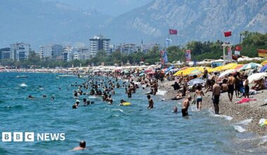 A beach in Turkey where lots of people are sunbathing under umbrellas, and many other people are swimming in the sea