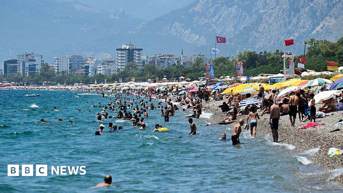 A beach in Turkey where lots of people are sunbathing under umbrellas, and many other people are swimming in the sea