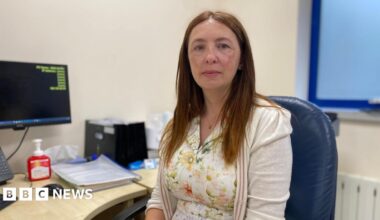 Dr Michelle Le Cheminant is wearing a white dress with patterned pale flowers and a creme cardigan. She has medium length light brown straight hair.