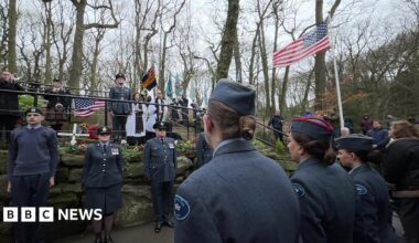 Members of the British and American military gather for a memorial service in a park - flags are flying including the stars and stripes