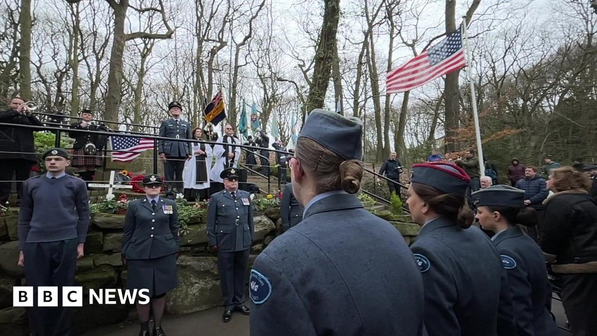 Members of the British and American military gather for a memorial service in a park - flags are flying including the stars and stripes