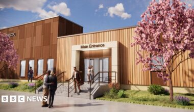 A computer generated image of what the new diagnostic centre will look like. It is a large rectangular building clad in wooden planks. There are a set of stone steps leading up to an entrance with automatic doors. There are two cherry blossom trees growing on either side of the entrance on a patch of grass and flowers.
