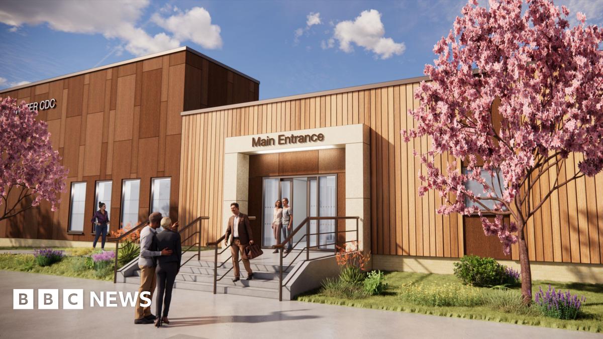 A computer generated image of what the new diagnostic centre will look like. It is a large rectangular building clad in wooden planks. There are a set of stone steps leading up to an entrance with automatic doors. There are two cherry blossom trees growing on either side of the entrance on a patch of grass and flowers.