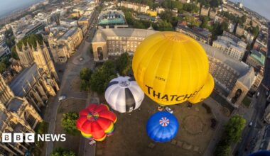 A group of colourful hot air balloons are seen from above as they take off from College Green in Bristol. The city's cathedral is visible on the left of the picture and other parts of the city are visible in the background