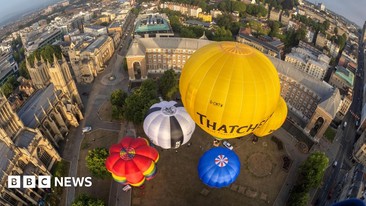 A group of colourful hot air balloons are seen from above as they take off from College Green in Bristol. The city's cathedral is visible on the left of the picture and other parts of the city are visible in the background