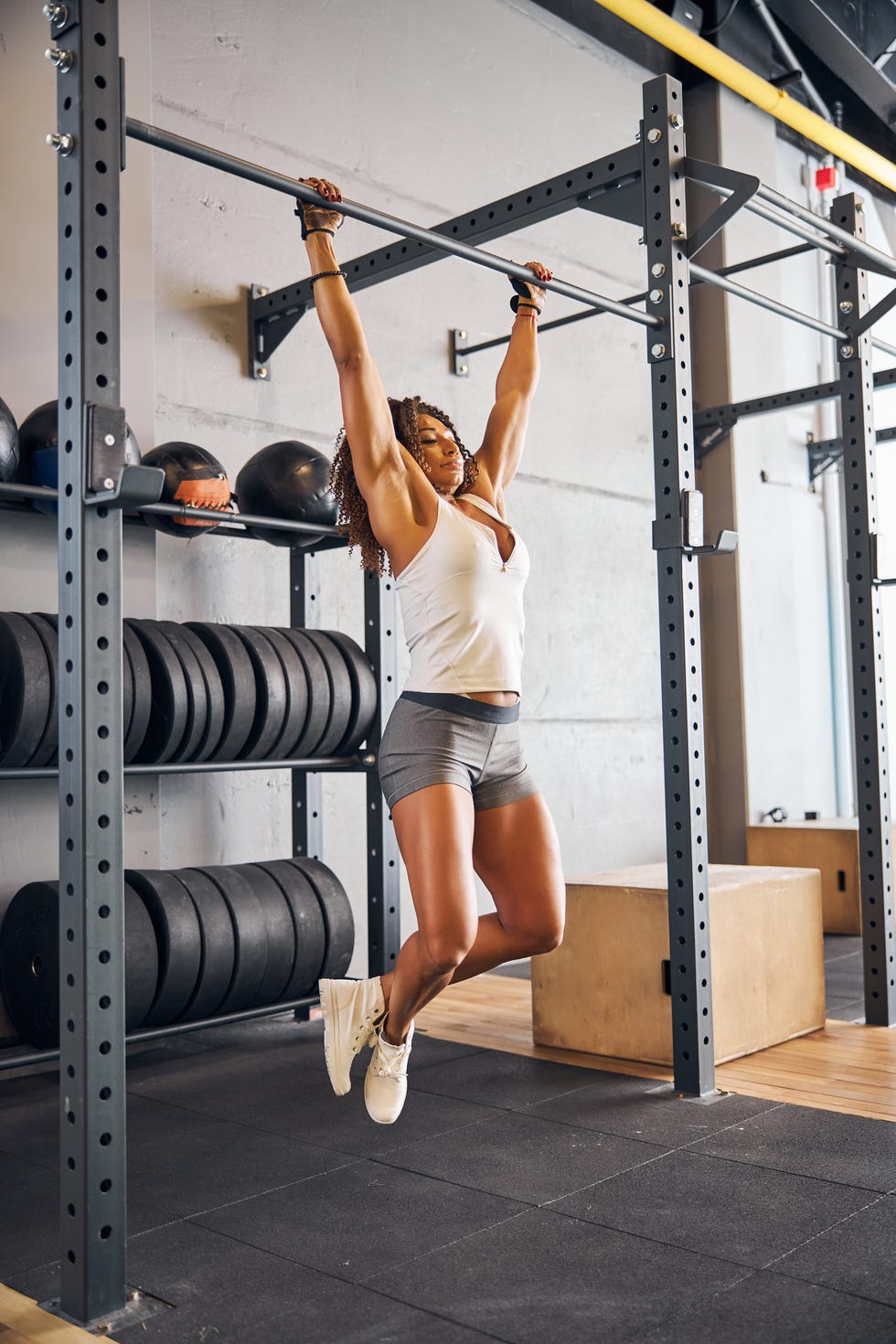serious female athlete hanging with her legs crossed and arms extended from the pull up bar