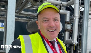 Aviation Minister Mike Kane stood in front of a network of pipes and machinery at the University of Sheffield's Advanced Manufacturing and Research Facility, wearing a high-visibility jacket and cap.