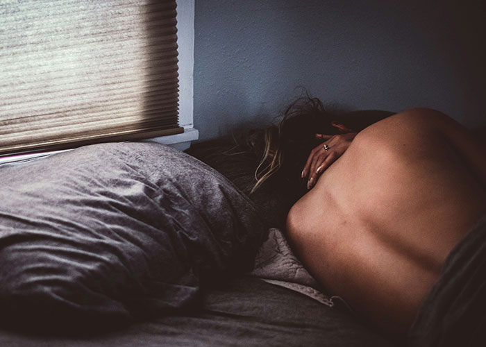 Person lying face down on a bed in a dimly lit room, illustrating patients who delayed help with shocking consequences.