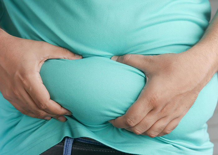 Person in a turquoise shirt holding their stomach, illustrating patients delaying help with shocking health consequences.