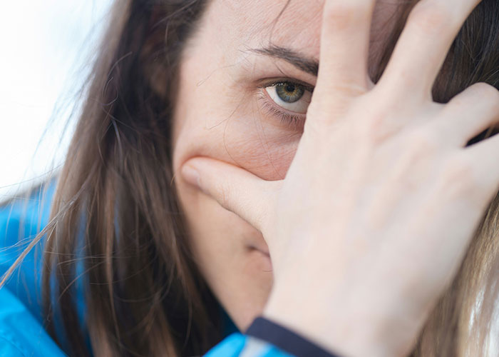 Close-up of a worried woman partially covering her face, reflecting the impact of delayed help in medical situations.