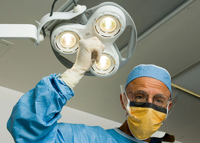 Surgeon adjusting surgical light in operating room, highlighting risks of patients delaying medical help and consequences.