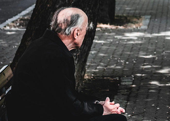 Elderly man sitting alone on a bench outdoors, reflecting on delayed help and its shocking consequences.