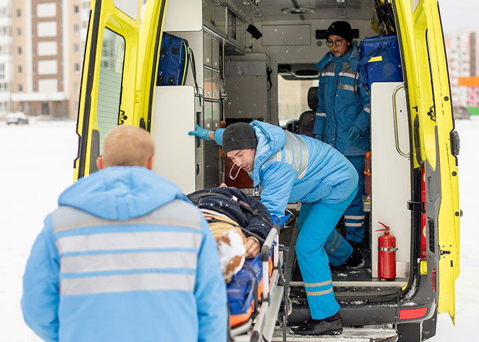 Emergency medical team loading patient into ambulance outside during snowy weather, highlighting delayed patient help consequences.