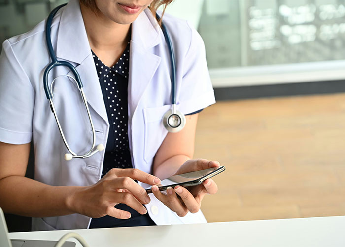 Female doctor in white coat using smartphone, highlighting consequences of patients delaying medical help and care.