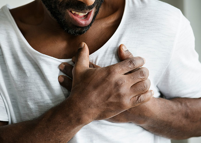 Man clutching chest in pain, illustrating patients delaying help with shocking health consequences and symptoms.