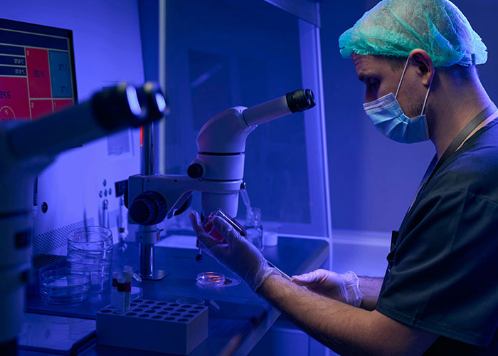 Medical professional in protective gear examining samples under microscope highlighting patients delayed help consequences.