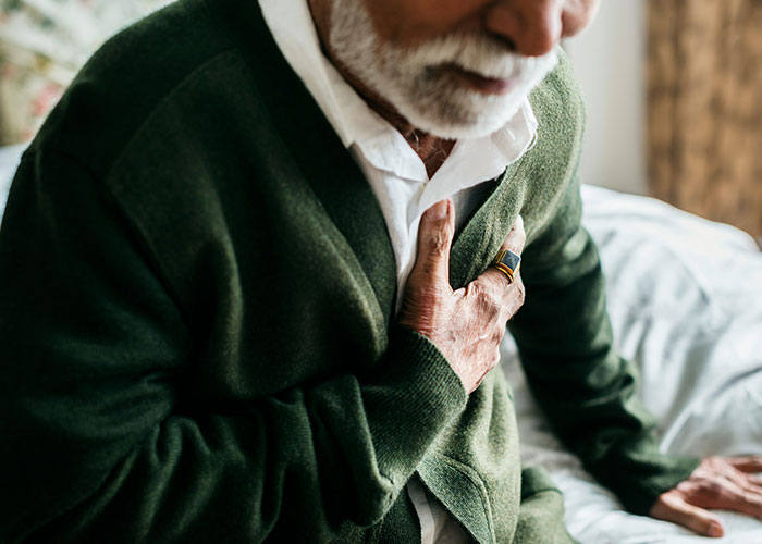 Elderly man clutching chest in pain, illustrating patients delaying help with shocking medical consequences.