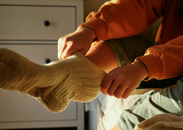 Person wearing beige knitted socks on bed, illustrating patients delaying help with shocking consequences in healthcare.