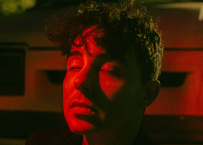 Person with eyes closed illuminated by red light, conveying emotions of delay and shock related to patients' health consequences.