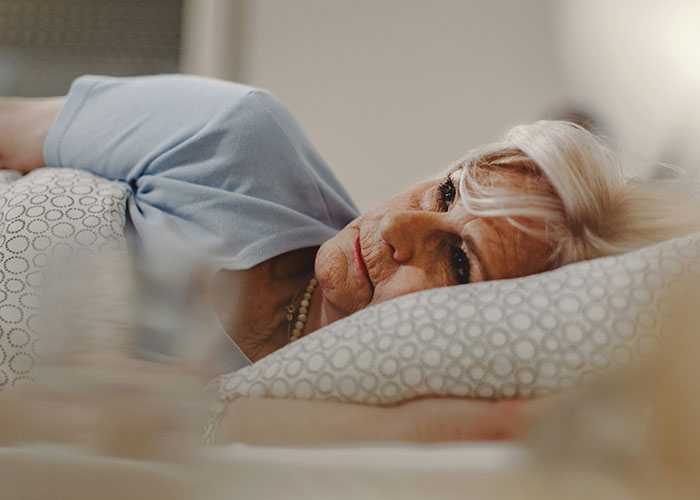 Elderly woman lying awake in bed, looking unwell and reflecting delayed help with shocking patient consequences.