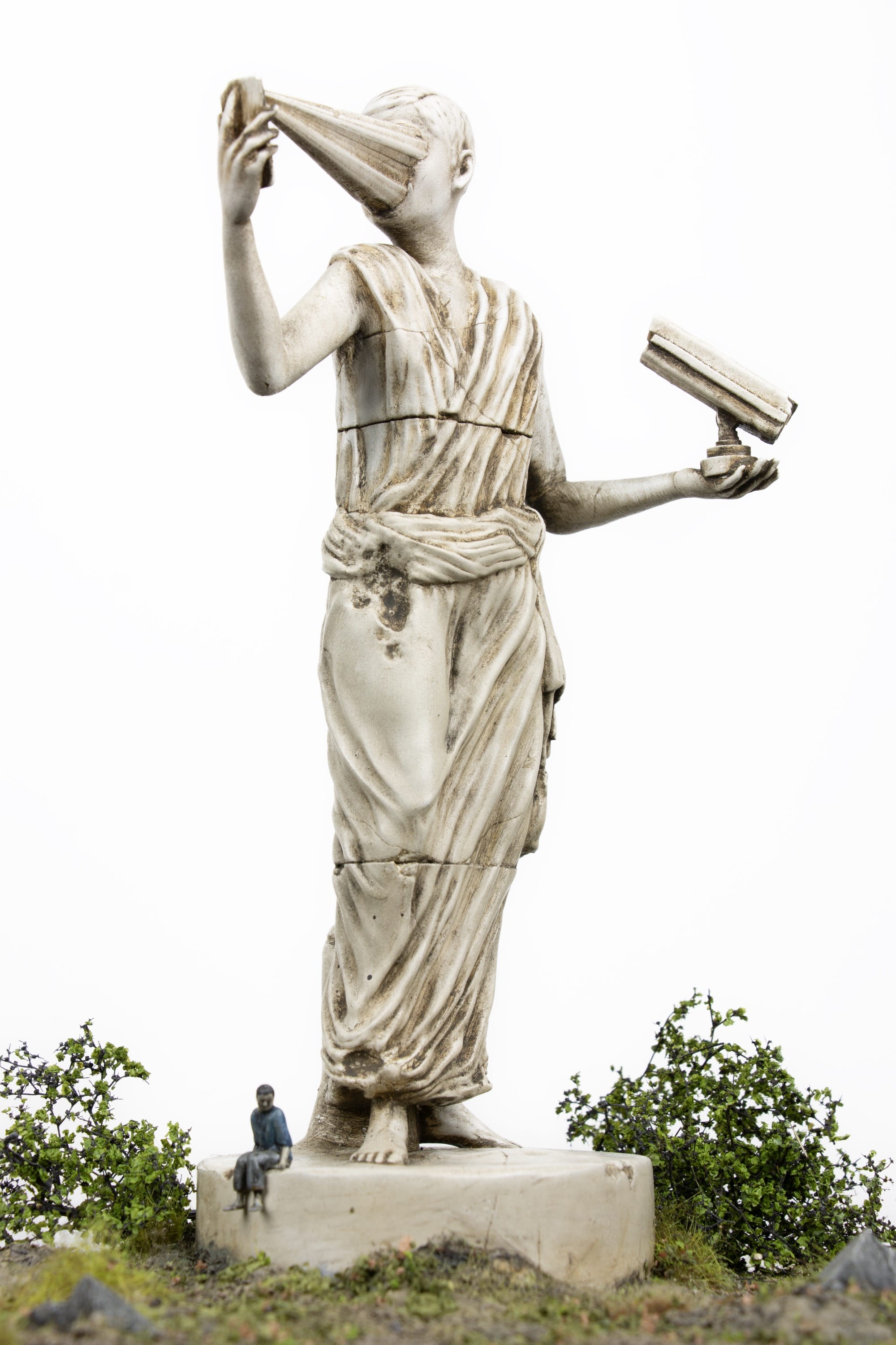 a miniature person sitting at the base of a figurative statue whose face melds into a phone